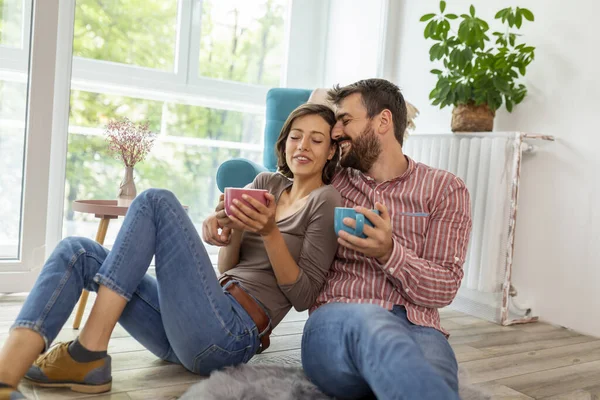 Güzel, birbirine aşık genç bir çift evde dinleniyor, sarılıyor, gülüyor ve sıcak çay içiyor.