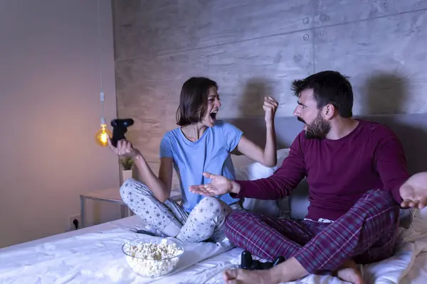 Pijama giyen, evde eğlenen, geceleri oyun oynayan, oyunu kazandıktan sonra heyecanlanan erkek hayal kırıklığına uğrayan genç bir çift.