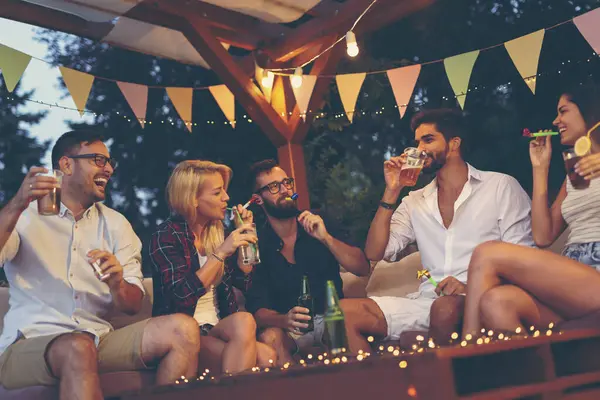 Bir grup genç arkadaş parti düdüğü çalıyor, bira içiyor ve açık hava yaz partisinde eğleniyorlar.
