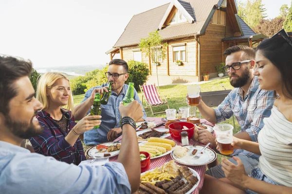 一群年轻的朋友一起吃着户外烧烤午餐 一边坐着一边敬酒 一边喝啤酒 — 图库照片