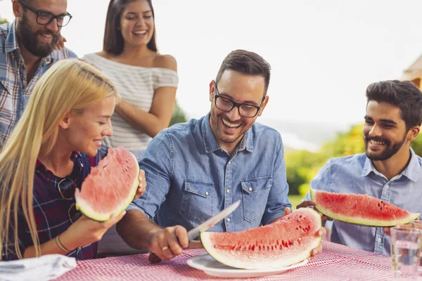 Bir grup arkadaş dışarıda öğle yemeği yiyor, taze karpuz dilimleri yiyor ve eğleniyorlar.