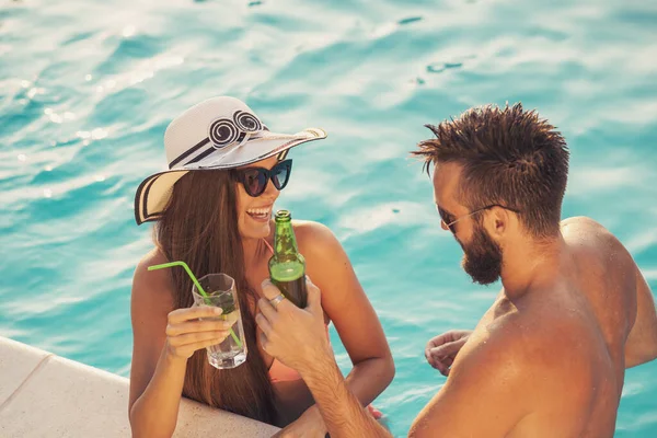 Havuz başında bir yaz partisinde aşık bir çift yüzme havuzunun kenarında duruyor, bira ve kokteyl içiyor ve eğleniyor.