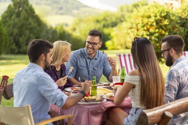 Bir grup arkadaş dışarıda barbekü yapıyor, ızgara et yiyor, bira içiyor ve eğleniyorlar. Ortadaki adama odaklan.