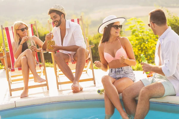 Group of friends at a poolside summer party, sitting at the edge of a swimming pool, drinking cocktails and beer and having fun. Focus on the guy sitting on the sunbed