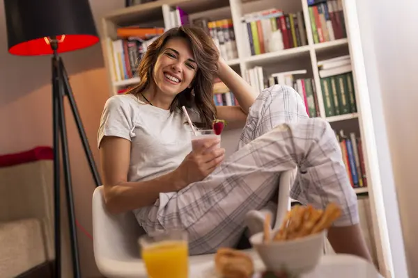 Güzel genç bayan hafta sonu sabahının tadını çıkarıyor, kahvaltı yapıyor ve taze çilekli smoothie içiyor.