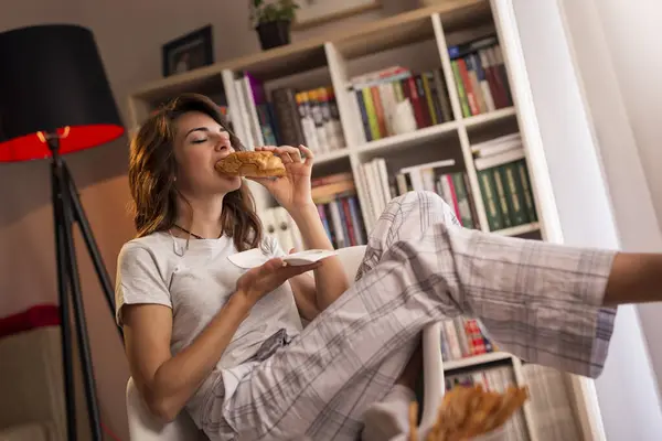 Güzel genç bir kadın pencerenin yanındaki sandalyeye oturmuş kahvaltıda taze kruvasan ve bir bardak portakal suyu içiyor.