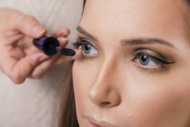 Makyaj stüdyosunda çalışan bir makyöz kadın müşterinin kirpiklerine rimel sürüyor.