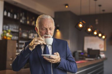 Restoran tezgahının yanında bir fincan kahve içen kıdemli bir işadamının portresi.