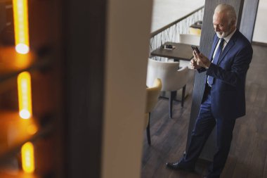 Modern bir ofis binasında duran kıdemli işadamı iş yerine gidiyor ve bir mesaj yazıyor.