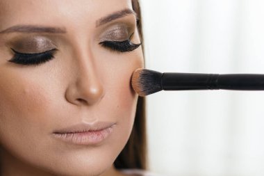 Makyaj sanatçısı makyajını yapıyor, makyaj fırçasıyla yüz pudrasını uyguluyor.