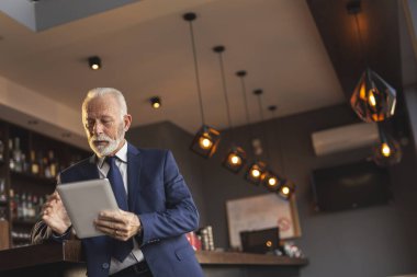 Modern bir ofis kafeteryasında duran kıdemli işadamı, bir tablet bilgisayar üzerinde çalışıyor.