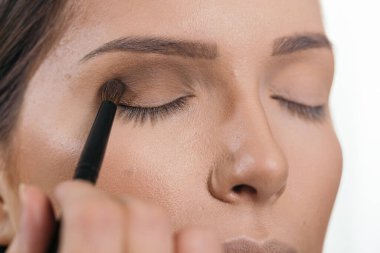 Makyaj stüdyosunda çalışan bir makyöz, kadın müşterinin göz kapaklarını gölgeliyor.
