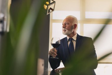 Bir kafede tezgahın yanında duran kıdemli işadamı yemek molasında şarap içiyor.