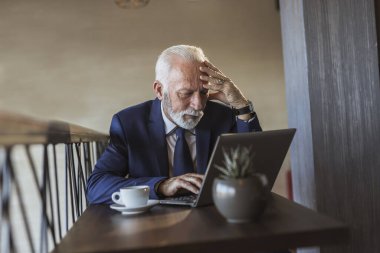 Restoran masasında oturan kıdemli işadamı, bir fincan kahve içiyor ve dizüstü bilgisayardan haber okuyor.