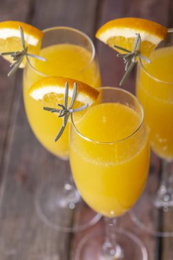 Portakal suyu ve lavanta yaprakları, çiçekler ve portakal dilimleriyle süslenmiş yüksek açılı mimoza kokteylleri.