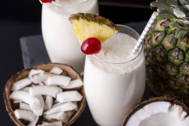 Koyu rom, ananas suyu ve Hindistan cevizi kremalı, ananas dilimleri ve maraska sosuyla süslenmiş iki bardak pina colada kokteyli.