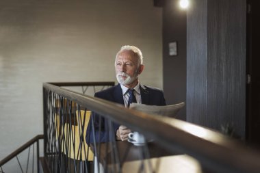 Restoran masasında oturan kıdemli işadamı gazete okuyor ve kahve içiyor.