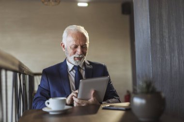 Restoran masasında oturan kıdemli işadamı, kahve içiyor ve tablet bilgisayar kullanarak iş haberleri okuyor, düşünceli ve ciddi.
