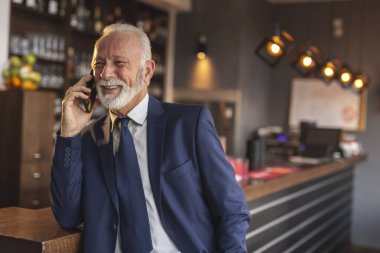 Üst düzey bir işadamı modern bir ofis binası tezgahının yanında duruyor ve telefon görüşmesi yapıyor.
