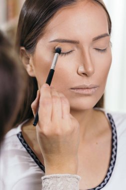 Makyaj stüdyosunda çalışan bir makyöz, kadın müşterinin göz kapaklarını gölgeliyor.