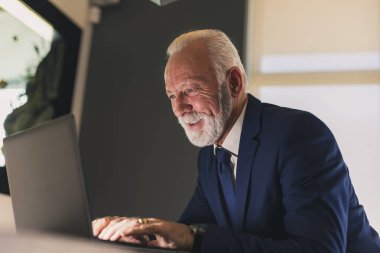 Modern bir ofiste çalışan kıdemli işadamı dizüstü bilgisayarına e-posta yazıyor.