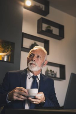 Bir restoranda kıdemli işadamı, dizüstü bilgisayarda çalışıyor ve bir fincan kahve içiyor.