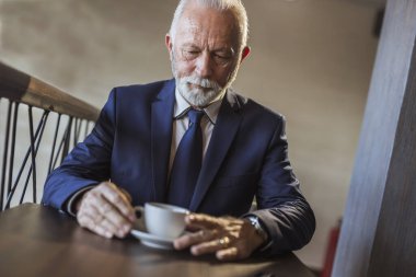 Kahve molasında kıdemli işadamı, restoran masasında oturuyor, kahve içiyor ve dinleniyor.