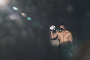Spor salonunda çalışan, maske takan ve ağırlık kaldıran kaslı vücut geliştirici.