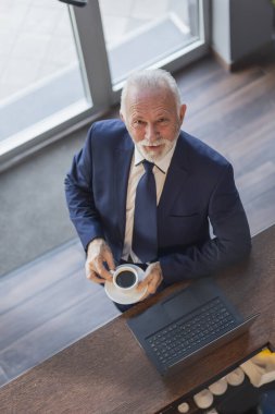 Üst düzey bir işadamının portresi. Restoran tezgahında duruyor, kahve içiyor ve dizüstü bilgisayarla çalışıyor.