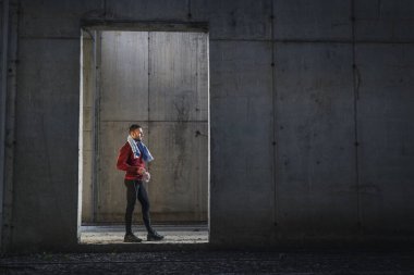 Spor kıyafetleri giyen kaslı bir adam spor yapıyor, su içiyor ve dinleniyor.