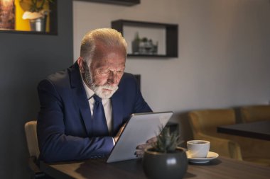 Bir restoranda kıdemli işadamı, tablet bilgisayarda çalışıyor, düşünceli ve ciddi.