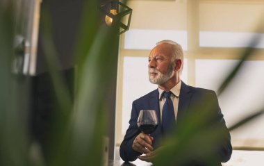 Bir kafede tezgahın yanında duran kıdemli işadamı yemek molasında şarap içiyor.