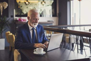 Restoran masasında oturan kıdemli işadamı, bir fincan kahve içiyor ve dizüstü bilgisayar üzerinde çalışıyor.