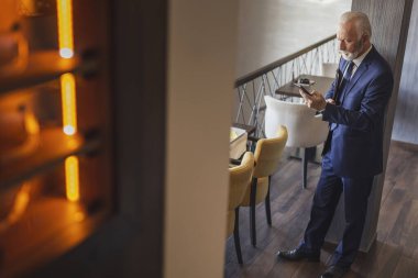 Modern bir ofis binasında duran kıdemli işadamı iş yerine gidiyor ve bir mesaj yazıyor.