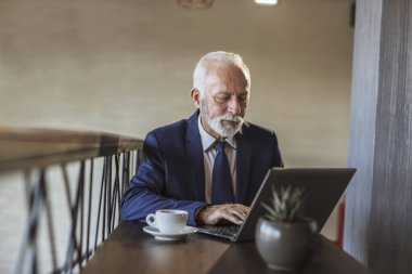 Restoran masasında oturan kıdemli işadamı, bir fincan kahve içiyor ve dizüstü bilgisayardan haber okuyor.