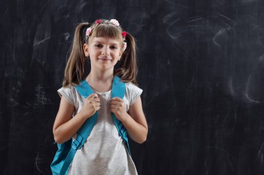 Sırt çantası takan liseli kız, okulun ilk gününde bir tahtanın önünde duruyor.