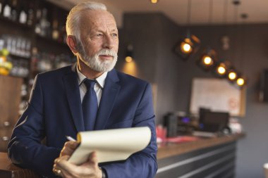Restoran müdürü tezgahın yanında duruyor, belgeleri tutuyor, satın alma ve tedarik sözleşmeleri imzalıyor.