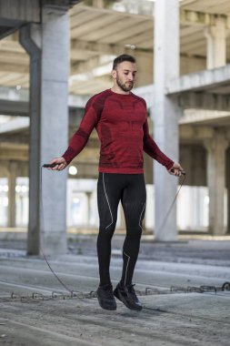 Atletik, kaslı adam atlama halatlarıyla çalışıyor. Sporcu atlama ipi kullanıyor, spor salonunda sıkı çalışıyor, kardiyo egzersizleri yapıyor.