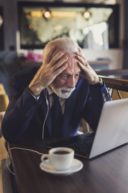 Restoran masasında oturan kıdemli işadamı, konferans görüşmesi yaparken endişeli.