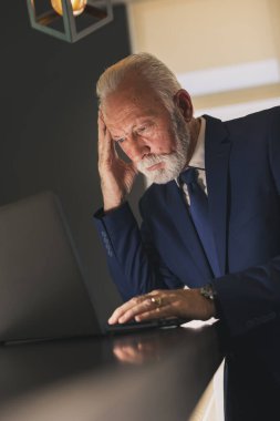 Modern bir ofiste kıdemli bir işadamı laptopta çalışıyor, düşünceli ve ciddi.