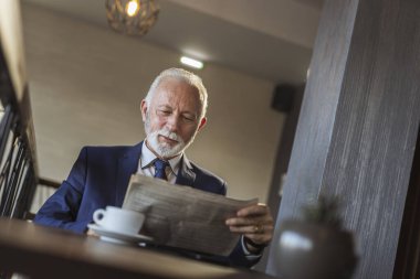 Üst düzey işadamı modern bir ofis binasında oturuyor, kahve içiyor ve gazete okuyor.