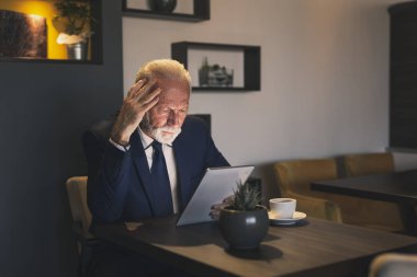 Bir restoranda kıdemli işadamı, tablet bilgisayarda çalışıyor, düşünceli ve ciddi.