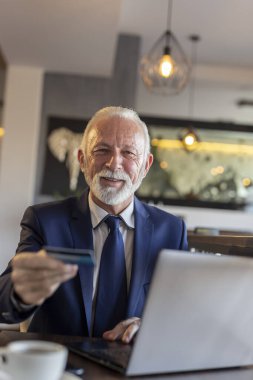 Restoran masasında oturan kıdemli işadamı, kredi kartını bir restoran çalışanına teklif ederek faturayı ödüyor.
