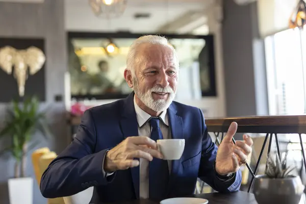 Senior businessman on coffee break in a restaurant, having a conversation with business partner and drinking coffee