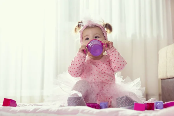 漂亮的小女孩穿着粉红短裙 坐在托儿所的地板上 喝着瓶子里的水 — 图库照片