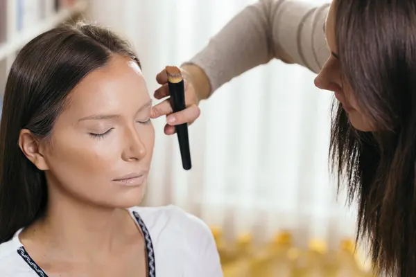 Make up artist applying liquid face powder foundation to a female client\'s face and blending contours