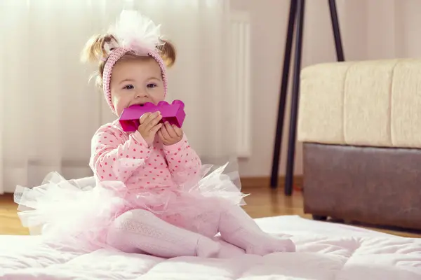 漂亮的小女孩穿着粉红短裙 坐在育婴室地板上的毛绒绒上 玩和咀嚼玩具块 — 图库照片