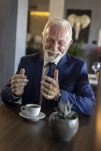 Senior businessman on a meeting in a restaurant, having a conversation with business partner and drinking coffee