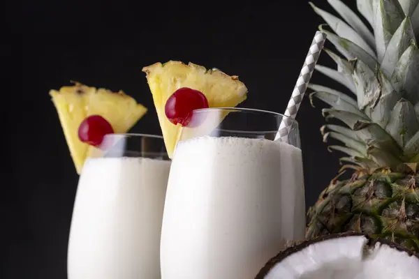 两杯黑朗姆酒 菠萝汁和椰子酱配以菠萝片和马拉西诺樱桃的凤梨鸡尾酒的细节 — 图库照片