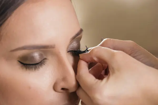 Make up artist working in a make up studio, putting artificial eyelashes on female client\'s eyelids